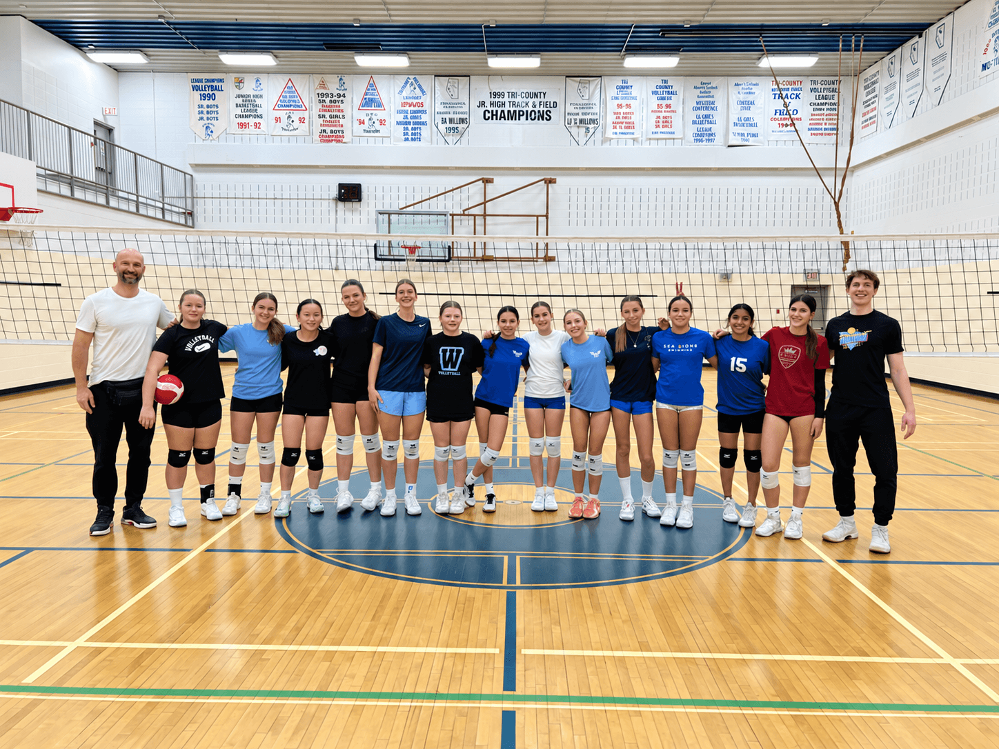 Youth volleyball team gathered by the net on an indoor court